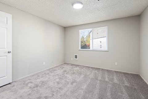 A room with a carpeted floor and a window showing a view of a house.