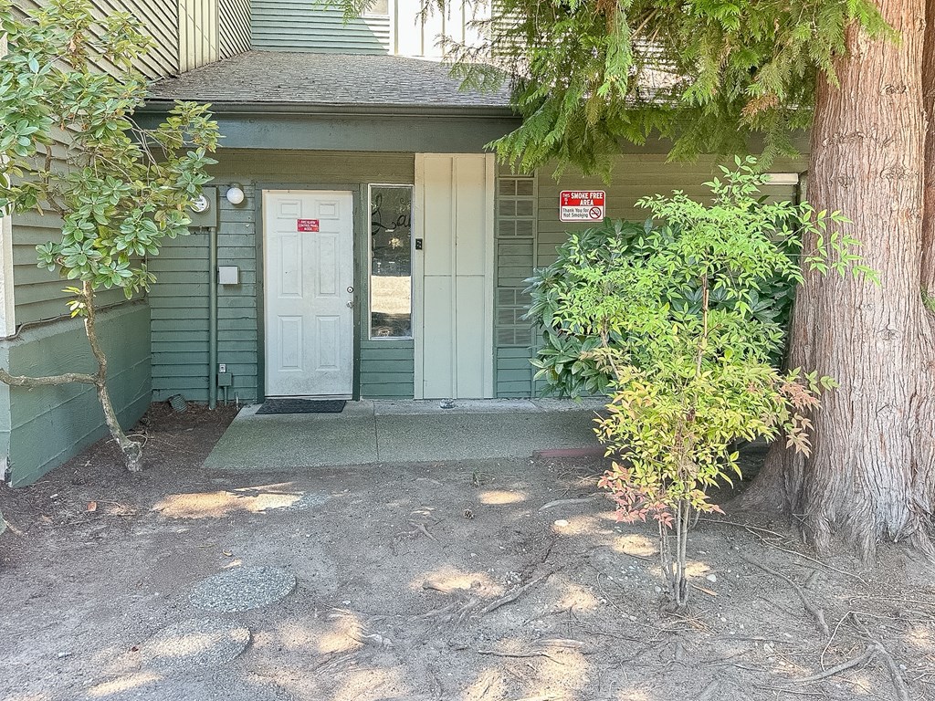 A small tree is planted in front of a green house.