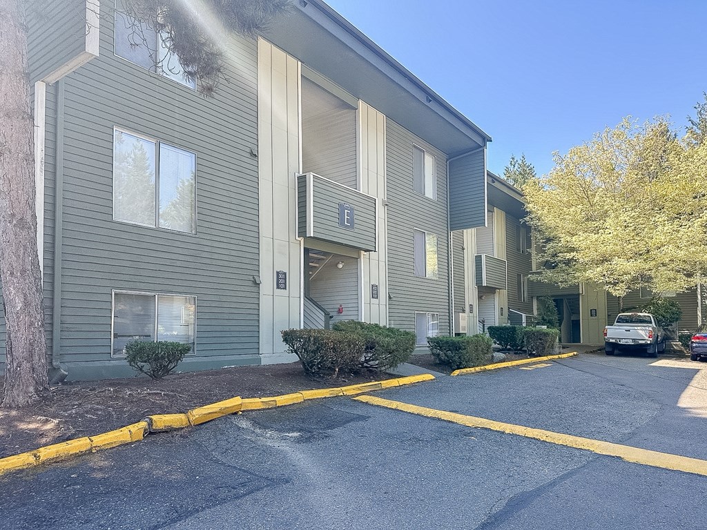 A parking lot in front of a grey apartment building.