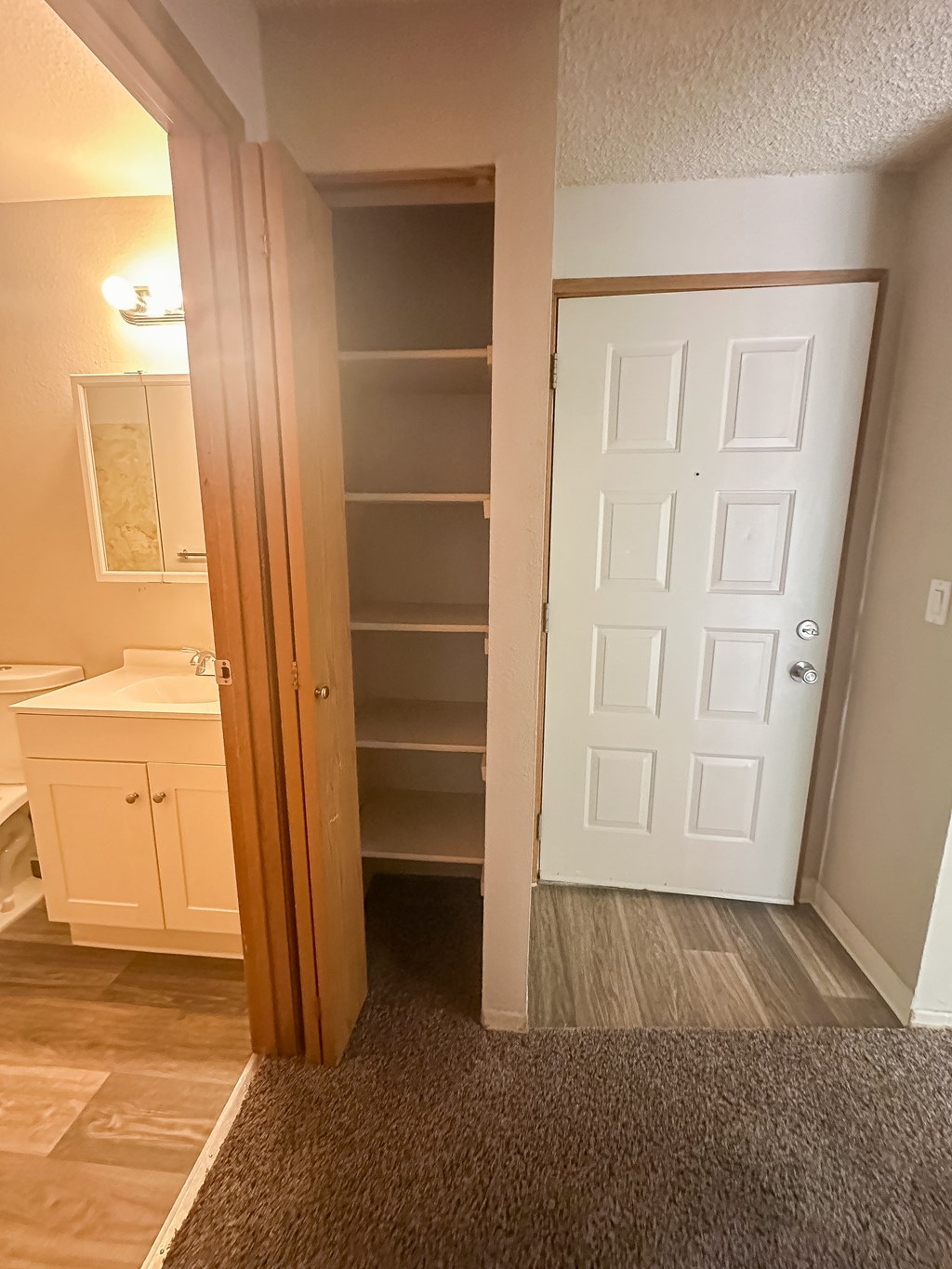 A white door is in a hallway with a white cabinet and a white sink.