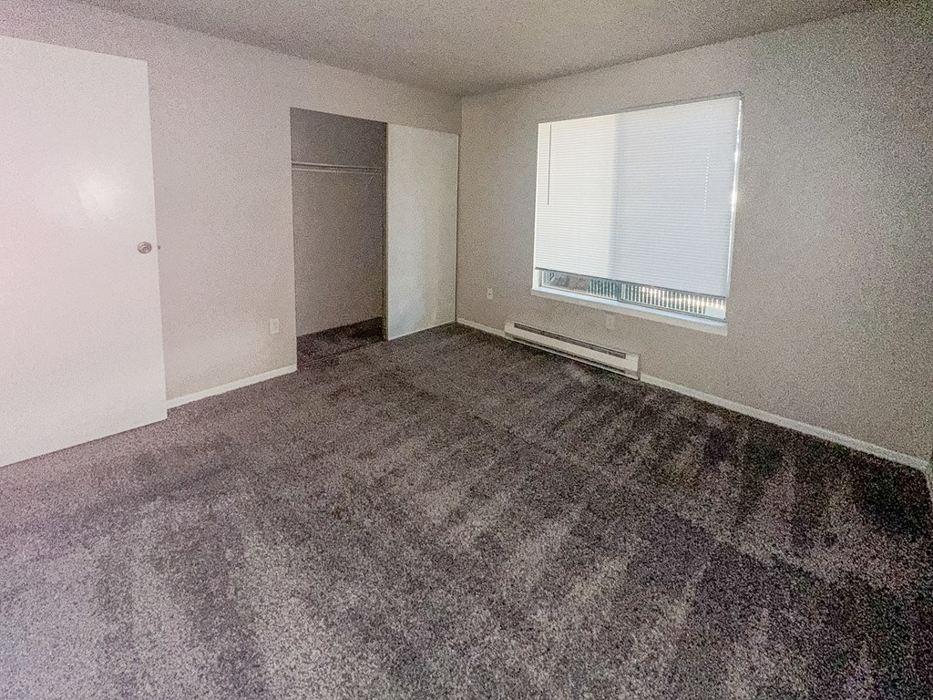 A room with a carpeted floor and a window with blinds.