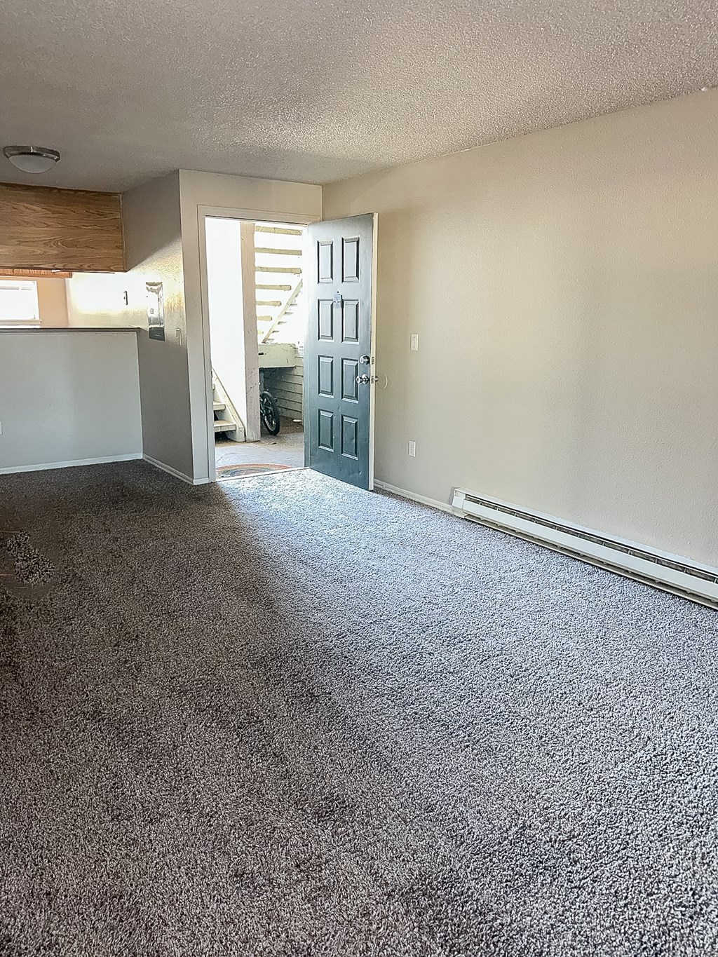 A room with a carpeted floor and a door leading to a staircase.