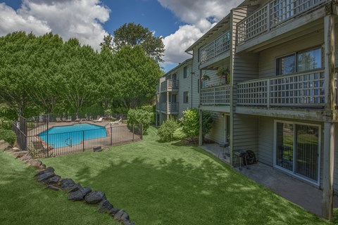 A large grassy area with a pool and a building in the background.