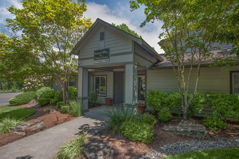 A small building with a porch surrounded by trees and plants.