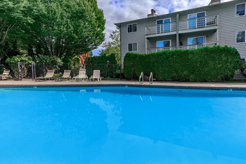 A swimming pool in front of a building with a green hedge.
