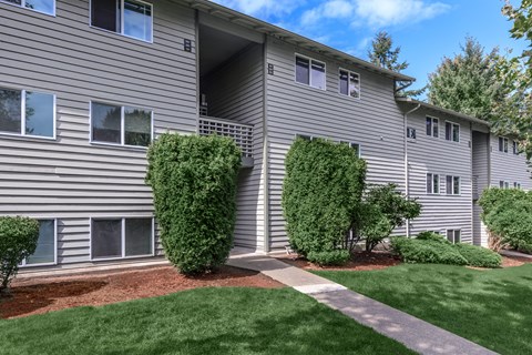 A building with grey siding and white trim with bushes in front.