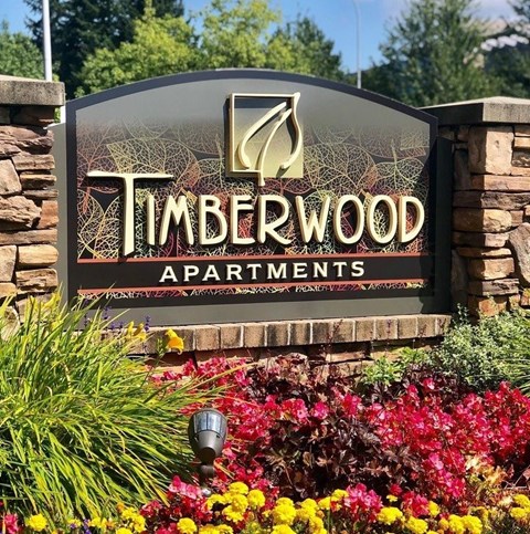 A sign for Timberwood Apartments is surrounded by flowers.