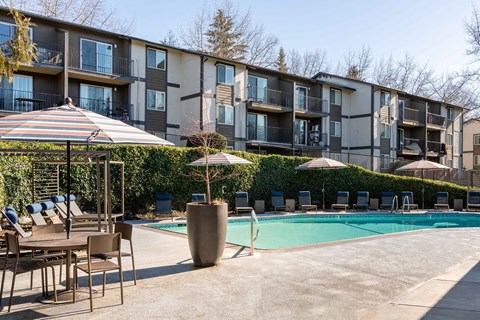 A pool area with chairs and umbrellas in front of apartment buildings.
