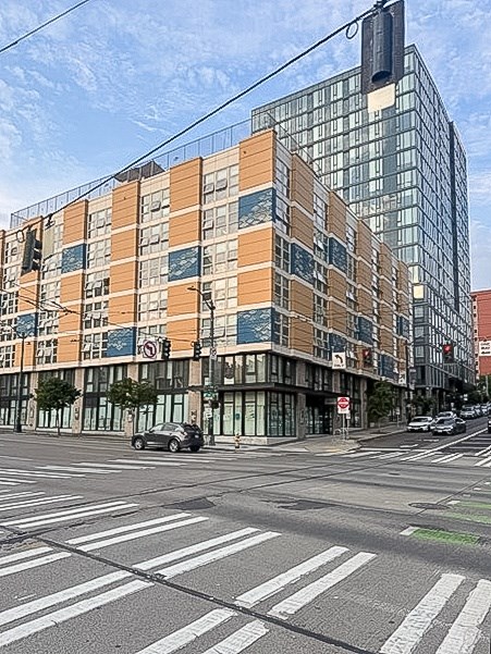 A modern building with orange and beige panels is situated on a street corner with a car parked on the side of the road.