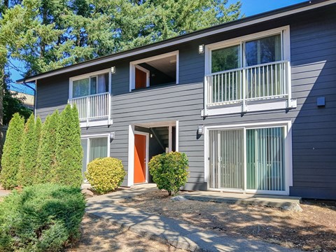 A grey two-story house with a red door and a balcony on the second floor.