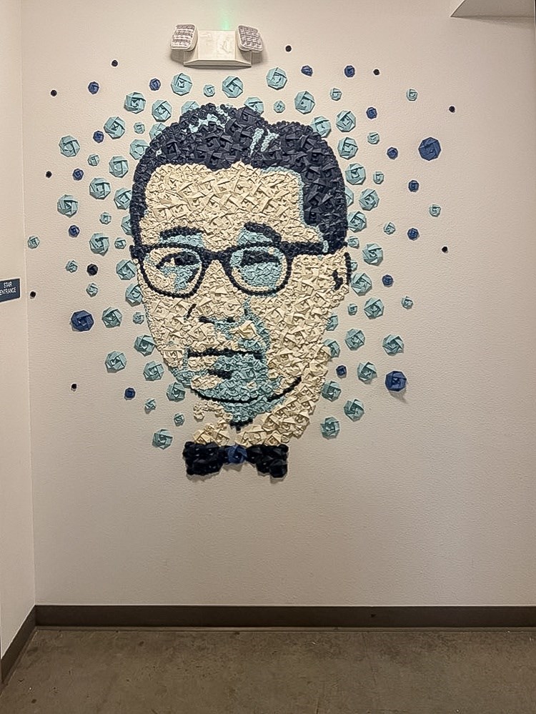 A portrait made of blue and black objects is on a white wall.