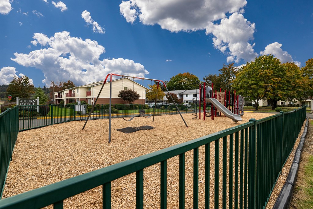 A playground with a green fence and a slide.