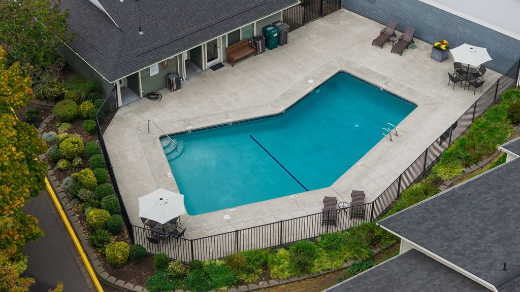 A small rectangular pool surrounded by a fence and a patio area with chairs and an umbrella.