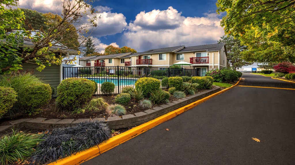 A road leads to a building with a pool and a fence.