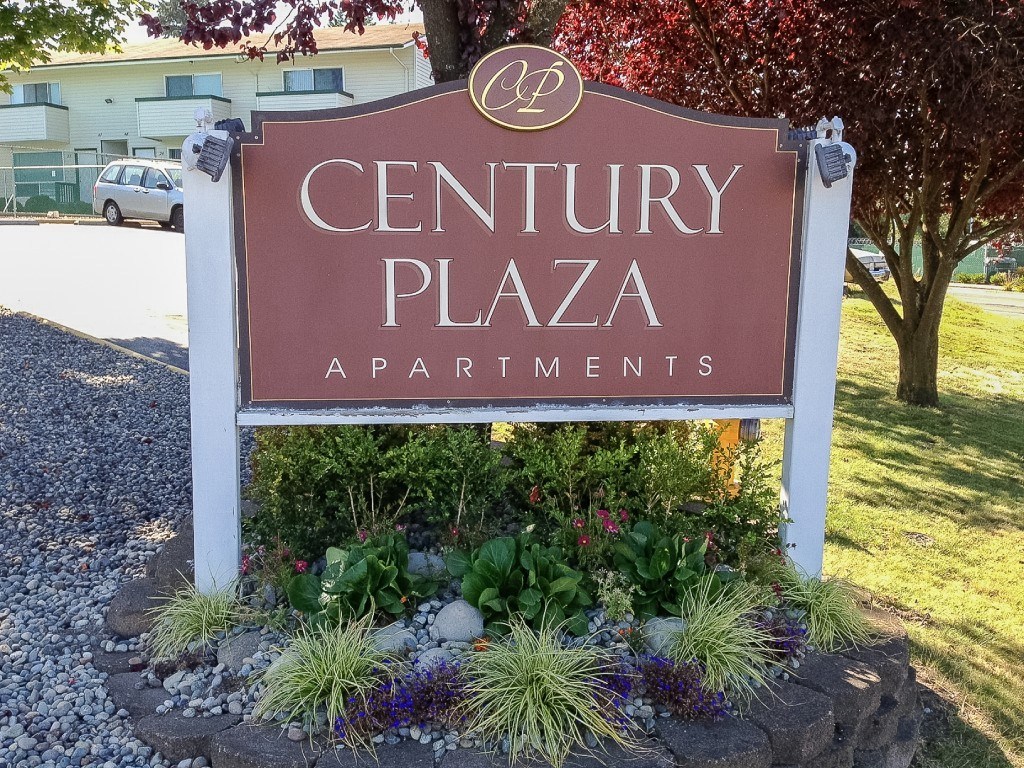 A sign for Century Plaza Apartments is surrounded by plants and flowers.