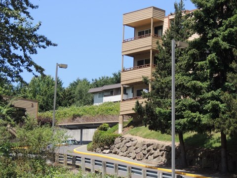 A modern building with balconies is surrounded by trees and greenery.
