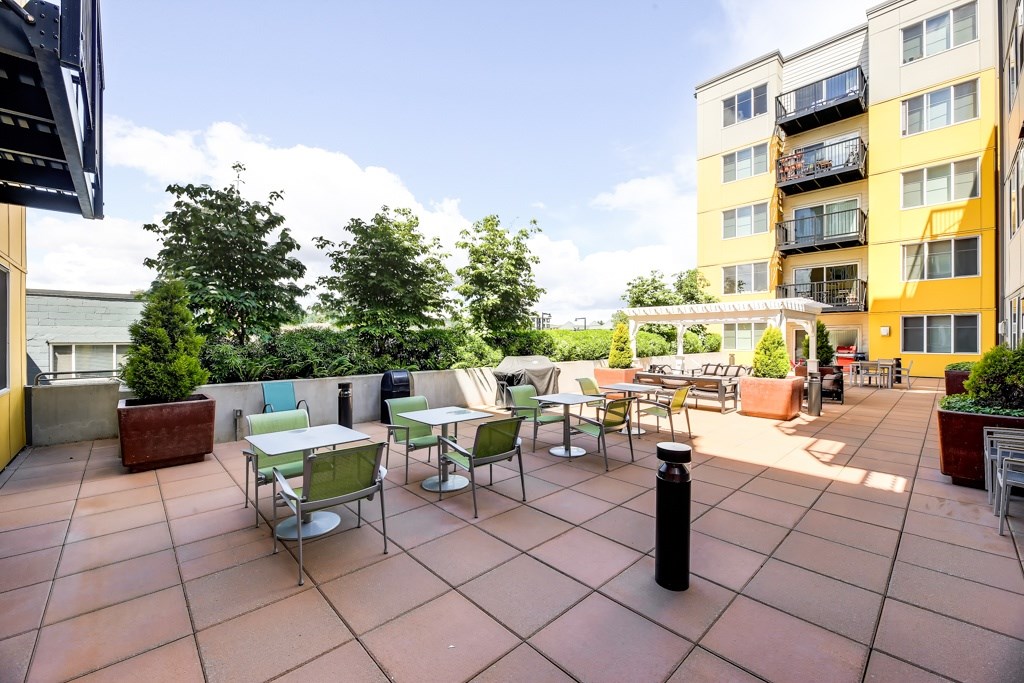 A patio with tables and chairs is surrounded by buildings.