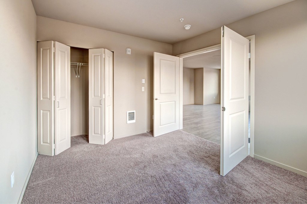 A room with a carpeted floor and white walls with a few open doors.