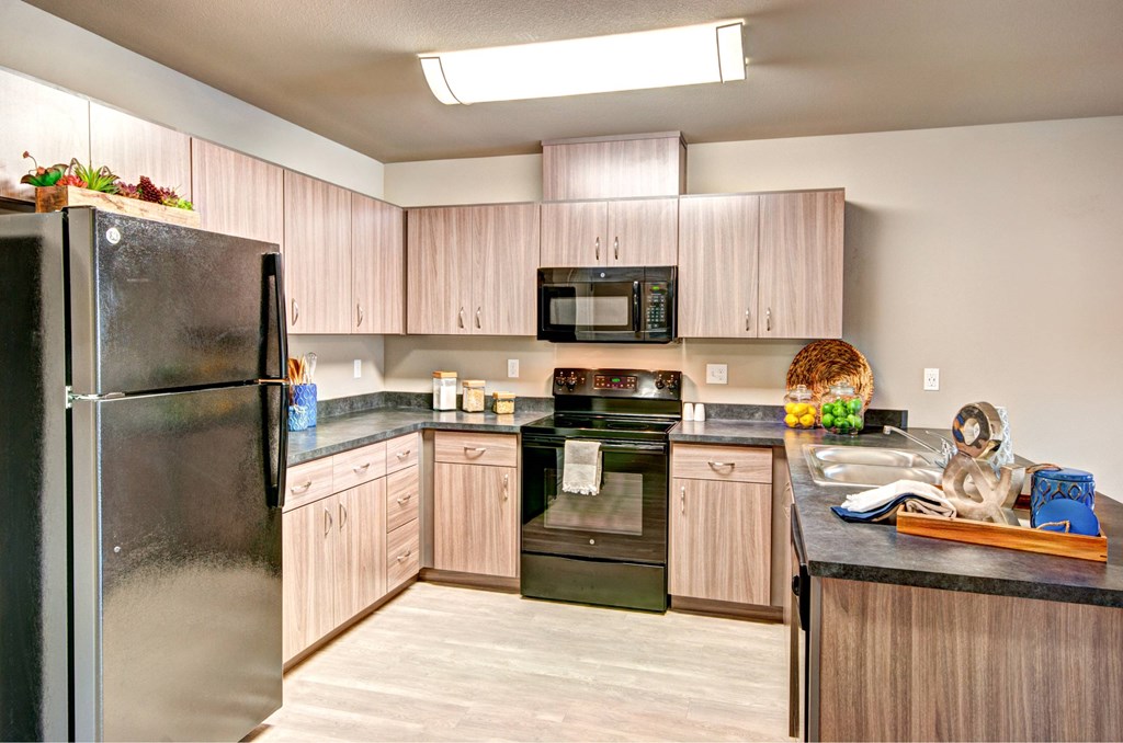 A kitchen with a black refrigerator and wooden cabinets.