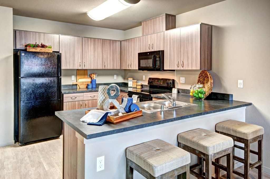 A kitchen with a black fridge, wooden cabinets, and a black stove top oven.