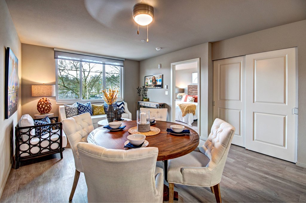 A dining room with a table set for two and a view of trees outside the window.