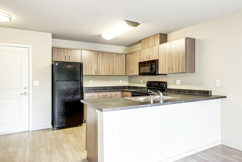 A kitchen with a black fridge and wooden cabinets.