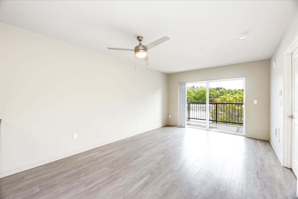 A spacious room with a ceiling fan and sliding glass doors leading to a balcony.