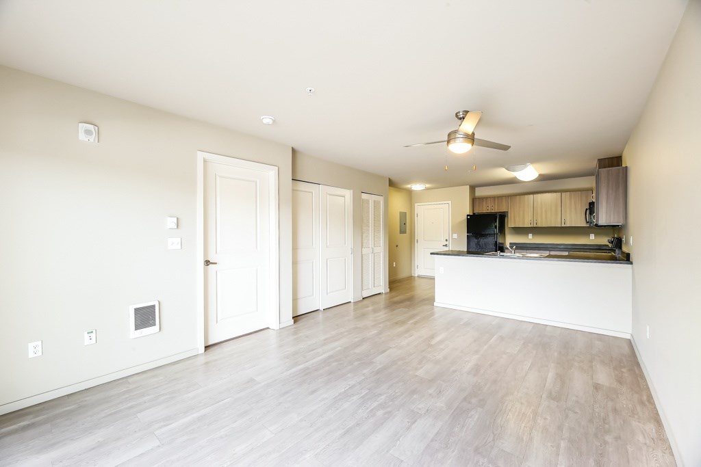 A spacious room with a kitchen area and a ceiling fan.