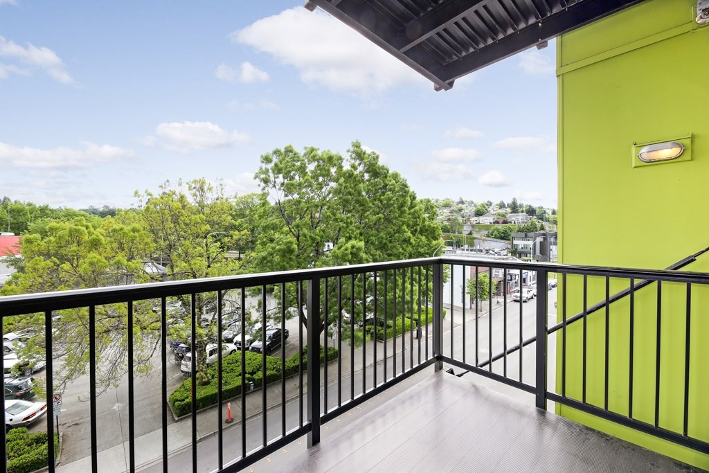 A balcony with a black railing and a view of a parking lot and trees.