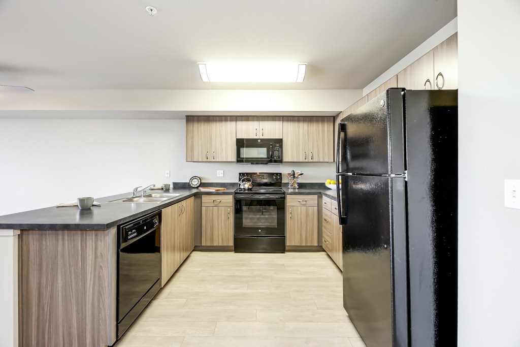 A modern kitchen with a black refrigerator and wooden cabinets.