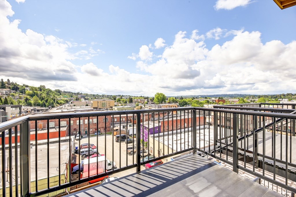 A balcony with a metal railing overlooks a parking lot and buildings.