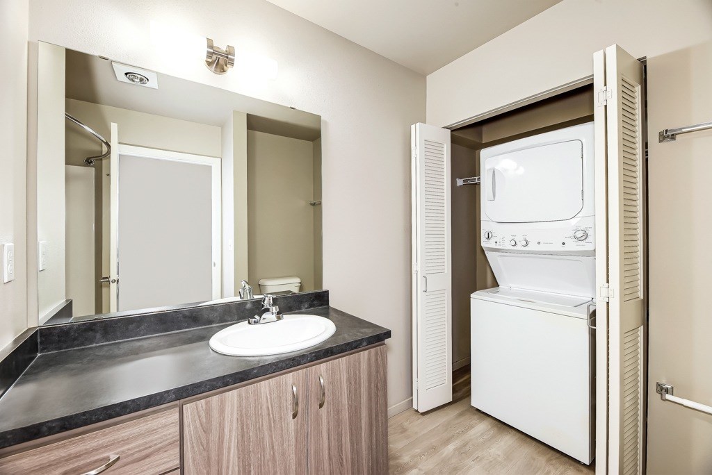 A bathroom with a sink, mirror, and a washer and dryer.
