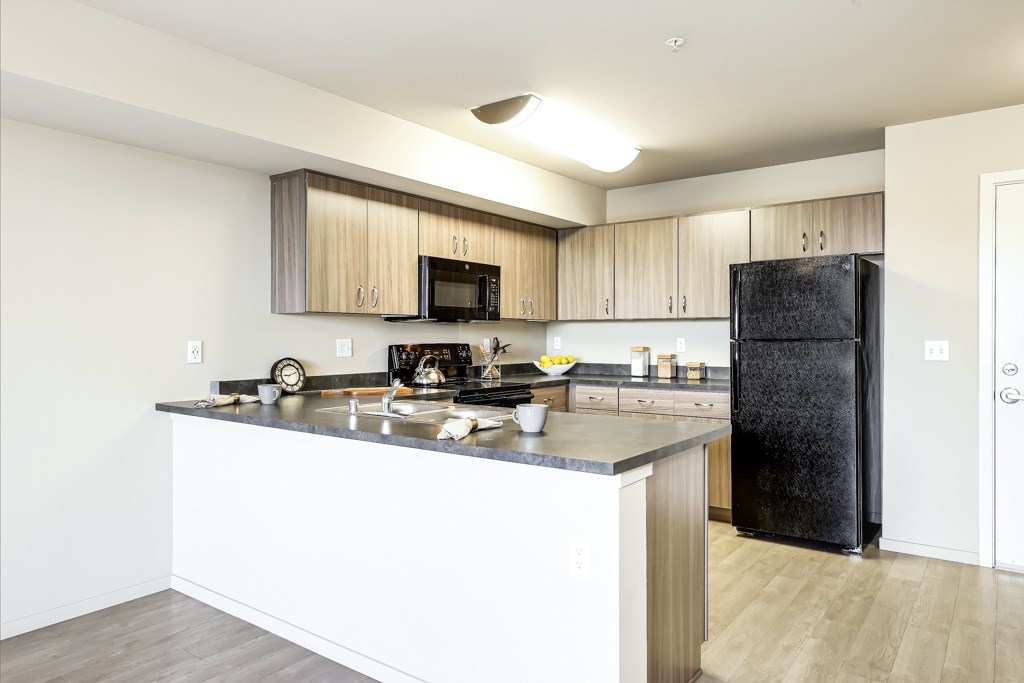A kitchen with a black refrigerator and white countertops.