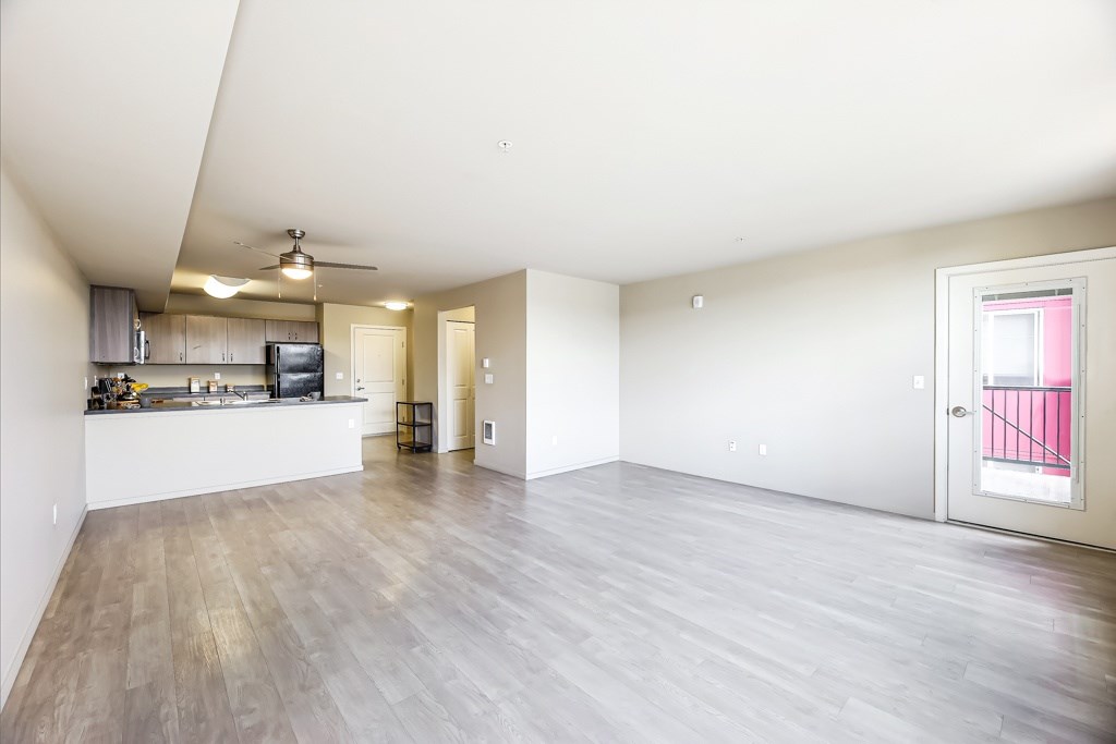 A spacious living room with a kitchen area and a ceiling fan.