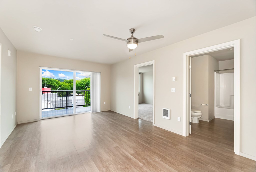 A spacious room with a ceiling fan and a view of a balcony with a railing.