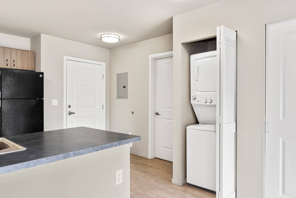 A black refrigerator sits next to a white washing machine in a kitchen.