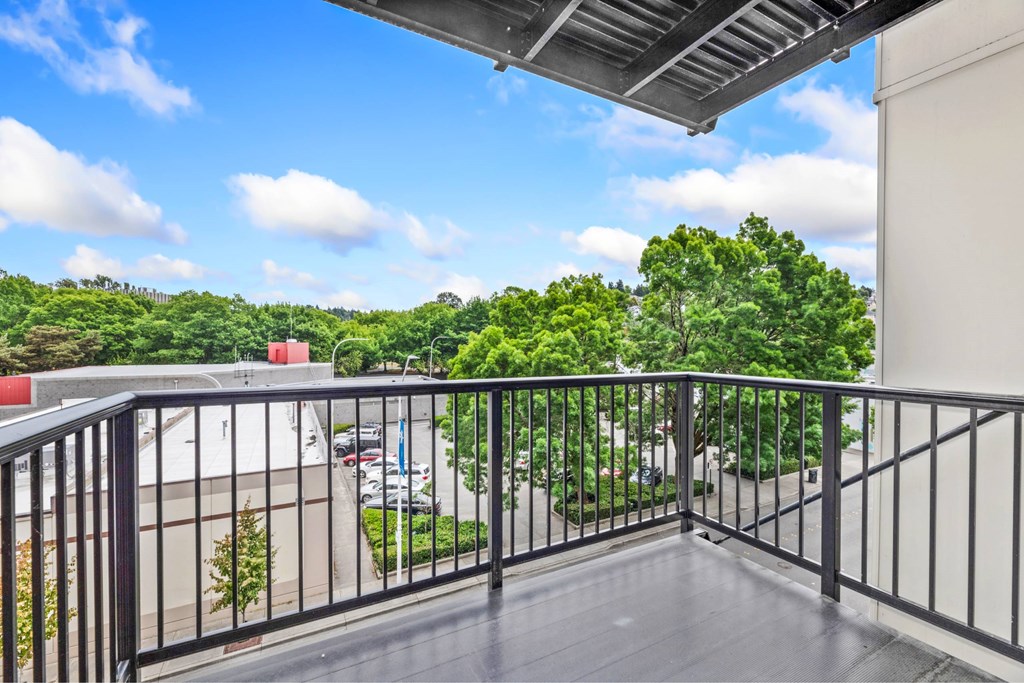 A balcony with a metal railing overlooks a parking lot and trees.