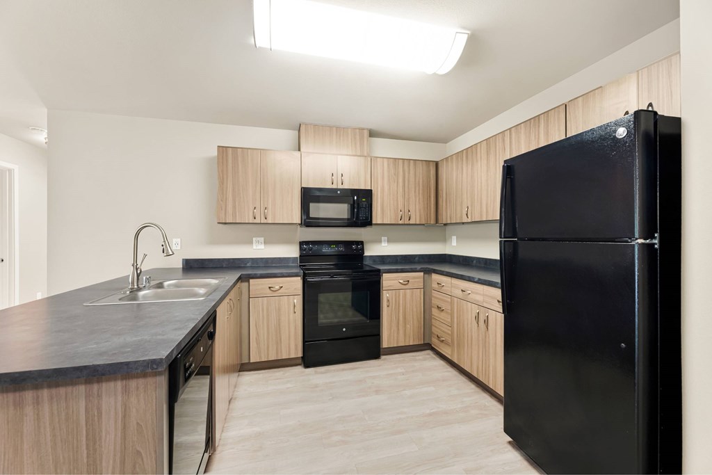 A black refrigerator stands in a kitchen with wooden cabinets and a black countertop.