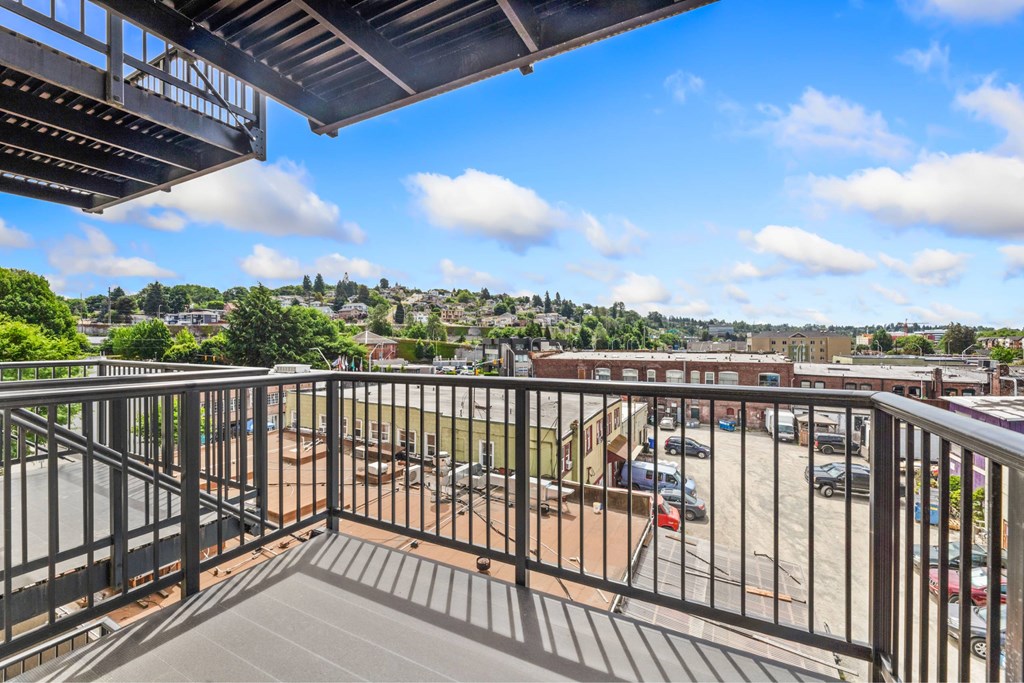 A balcony with a metal railing overlooks a parking lot and buildings.