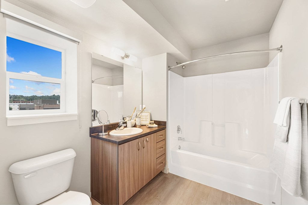 A white bathroom with a large window and a wooden vanity.