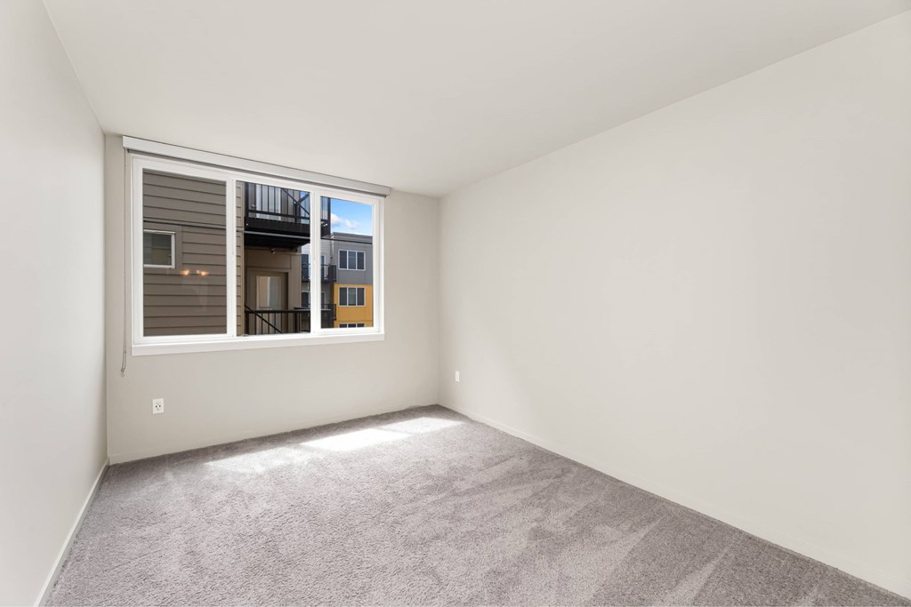 A room with a carpeted floor and a window showing a balcony and buildings outside.