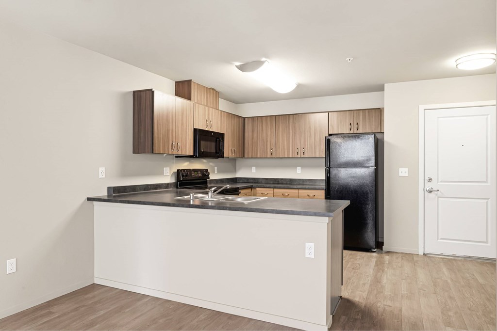 A kitchen with a black fridge and wooden cabinets.
