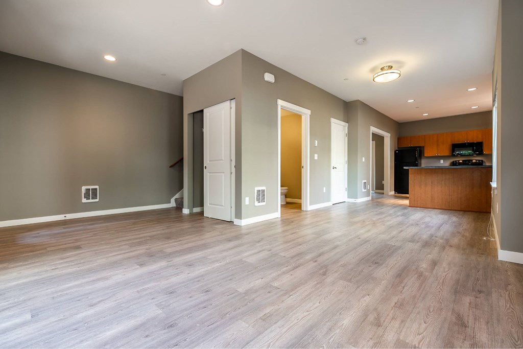 A spacious room with wooden floors and a kitchen area in the background.