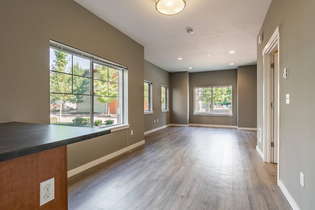 A large empty room with wooden floors and a window overlooking a tree-filled street.