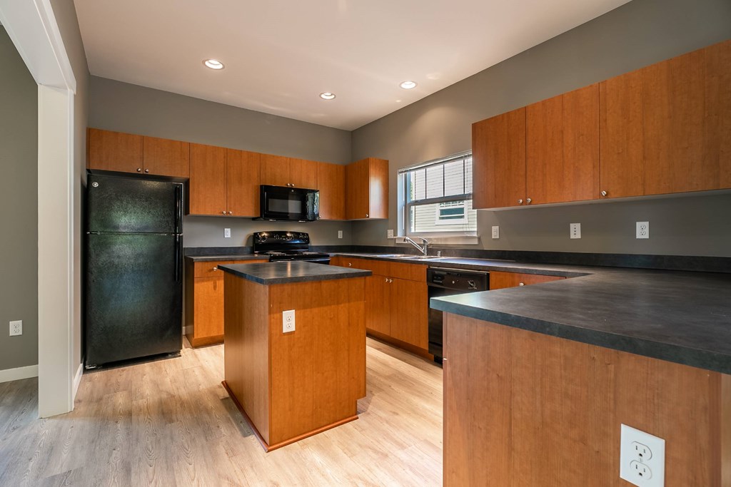 A kitchen with wooden cabinets and a black refrigerator.