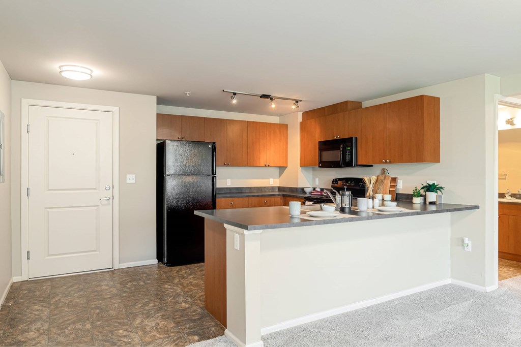 A kitchen with a black fridge and wooden cabinets.