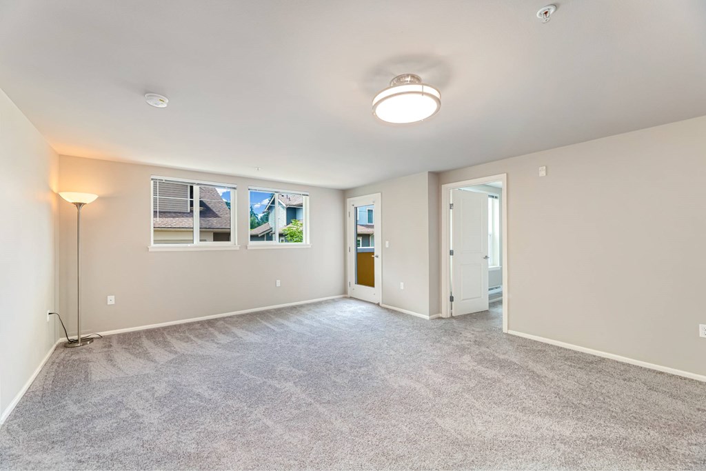 A spacious room with a carpeted floor and a window showing a view of other buildings.