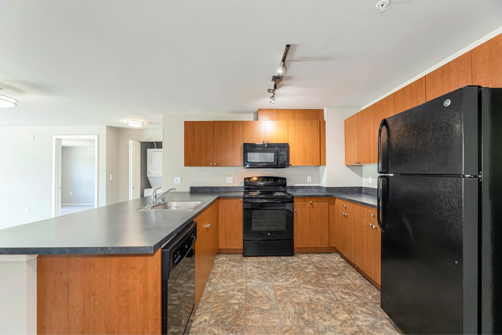 A black refrigerator is in the corner of a kitchen with wooden cabinets.