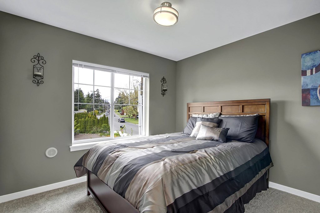 A bedroom with a bed, a window, and a painting on the wall.