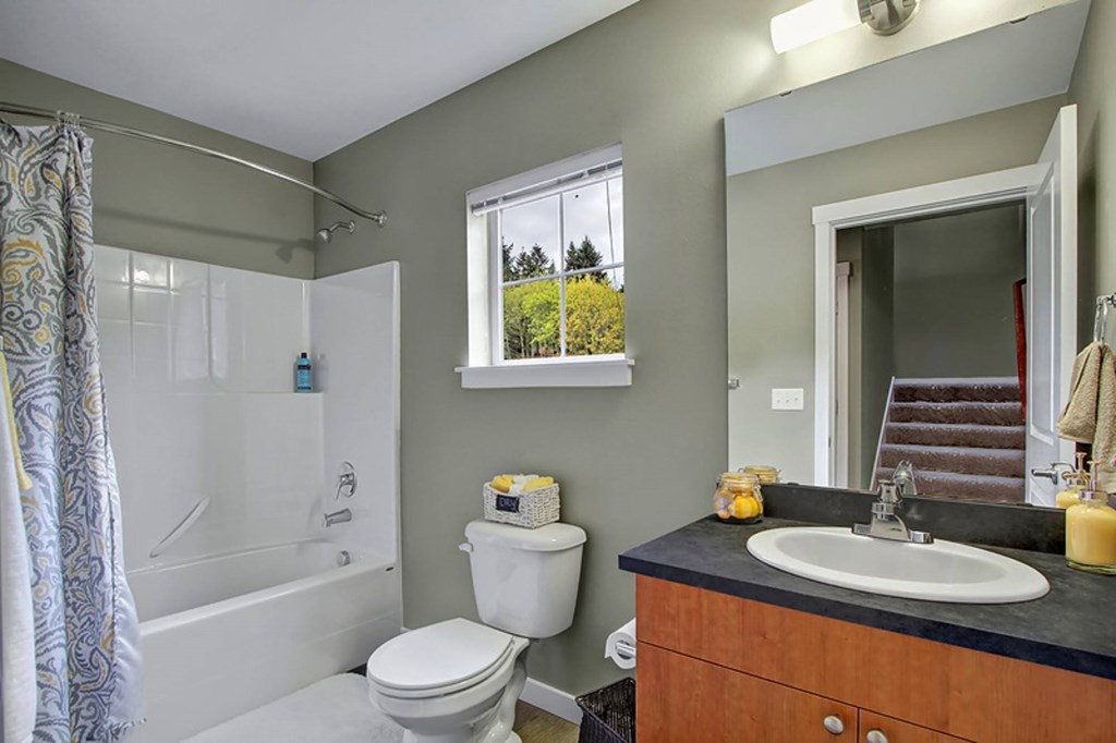 A bathroom with a white toilet, a black countertop, and a window with a view of trees.